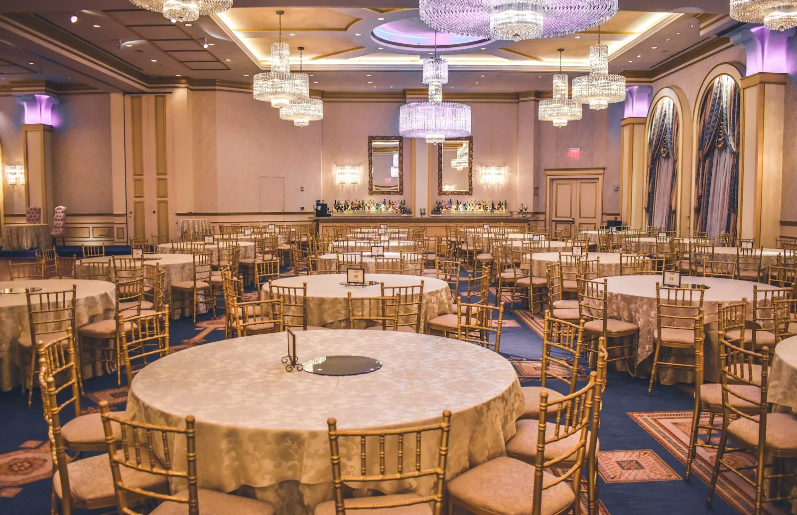 Formal gala dining hall prepared with round banquet tables, gold chairs and chandeliers