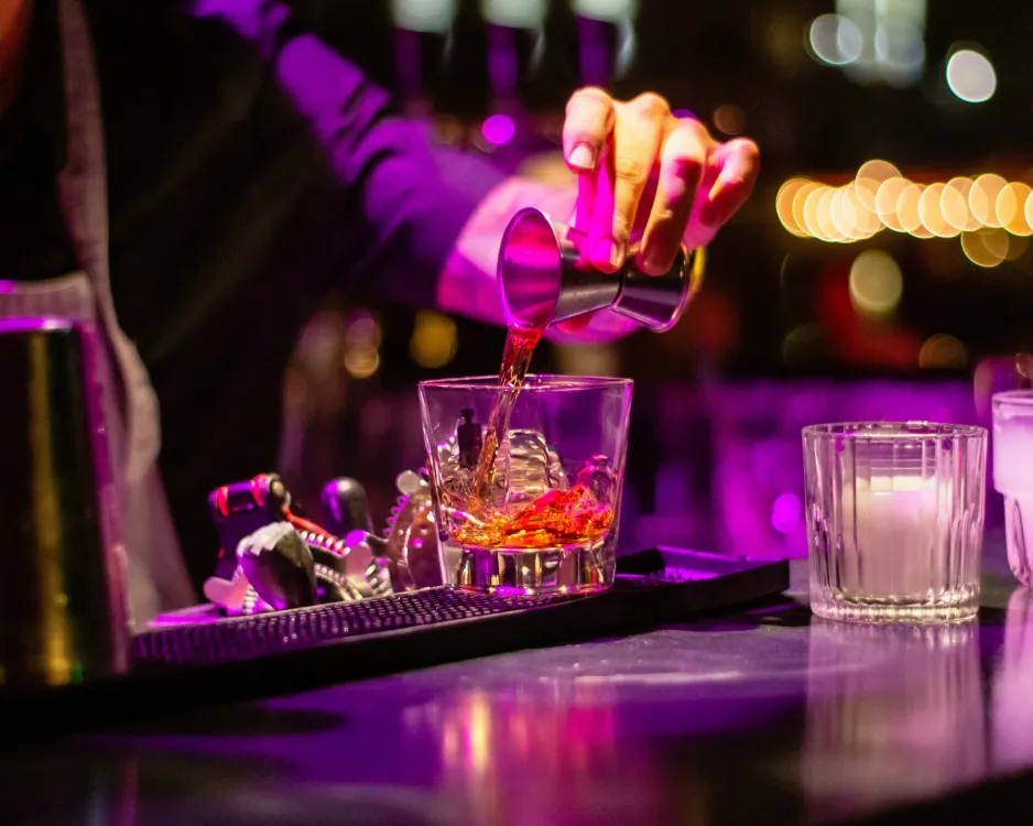 A bartender crafting a cocktail in colorful light