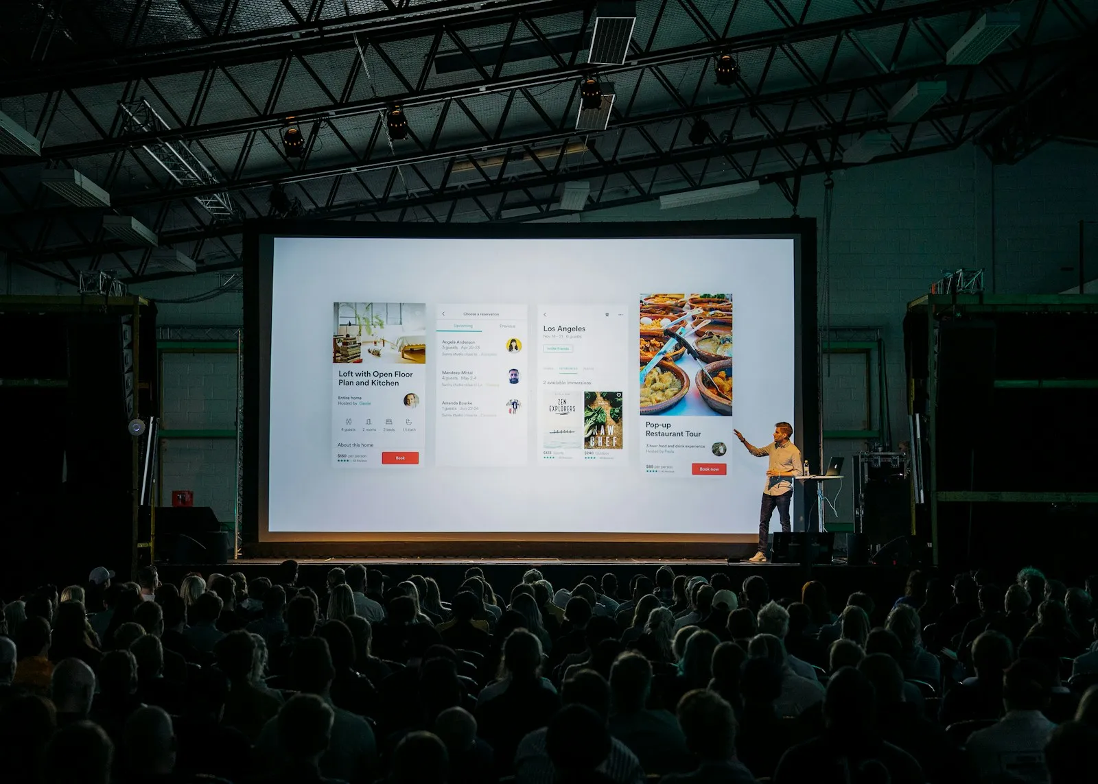 Conference speaker presenting to a seated business audience in a dark event hall